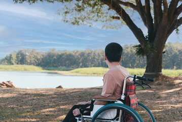 Back of young boy sitting on wheelchair looking at beautiful nature park, Traveling using a wheel...