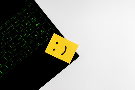 Top view of happy face sticky note on keyboard over wooden background.