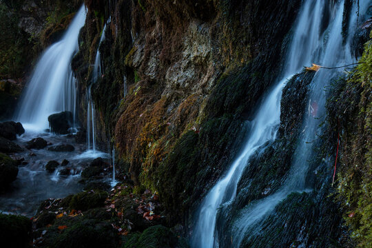 Silky streams of water cascade down a mossy cliff, surrounded by autumn leaves and the tranquil ambiance of a secluded spot