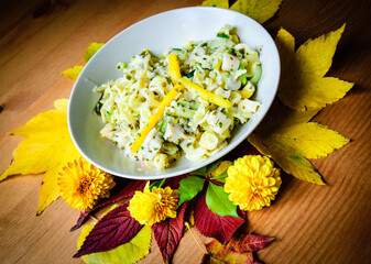 Delicious pasta with fish, scallops, green vegetables, herbs and yellow pepper with pesto sauce in bowl on old wooden table. Rustic decoration with autumn leaves and flowers. Healthy gourmet eating