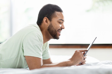 African american man using tablet in bed, using mobile app