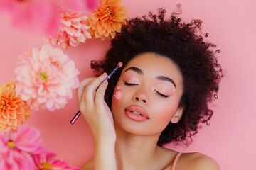 Portrait of attractive black woman applying eyeshadows with brush on pink background with flowers - obrazy, fototapety, plakaty