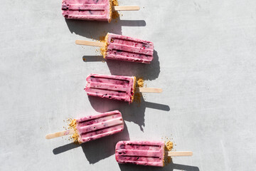 Homemade cherry yogurt pops in a line on a light surface in bright sunlight.