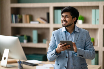 Happy Indian programmer man using tablet standing in modern office