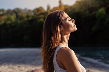 Young woman with long hair enjoying sun with closed eyes getting natural vitamin D outdoors. Peace of mind. Mindfulness, mental health,  spirituality, well-being, unwind yourself