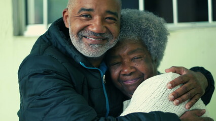 Adult South American black middle-aged son embracing elderly 80s gray-hair mother in loving tender hug depicting care and support in old age