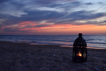 Decorative lantern with burning candles on the seashore at sunset