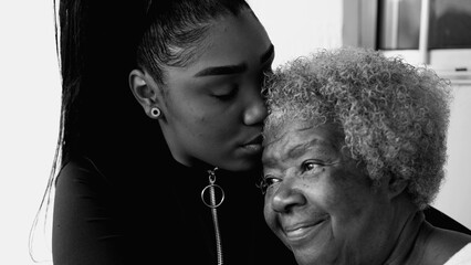 African American grandaughter kissing senior elderly grandmother in forehead in black and white,...
