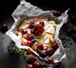 Melted baked Camembert cheese with cranberry sauce and fresh rosemary on a black background, focus on the middle - 757428862