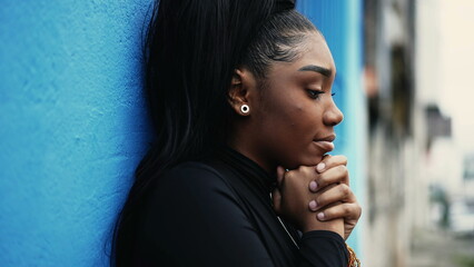 One pensive young black woman pondering decision with hands clenched together standing outside with...