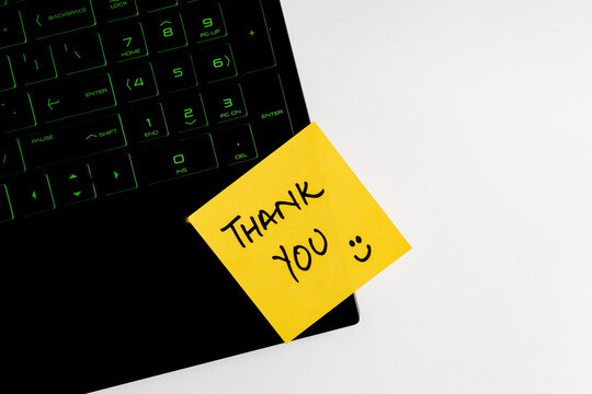 Top view of words Thank You written on sticky note on keyboard over wooden background.