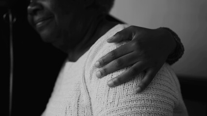 Close-up hand of family member around elderly grandmother's shoulder showing help and support in...