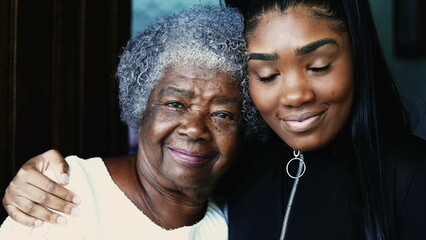 Happy portrait of young African American granddaughter with arm around her grandmother posing for camera, close-up faces of intergenerational family members embrace