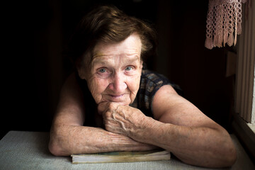 Portrait of a smiling wrinkled old lady sitting in a poor house. - 757436034