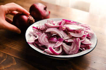 Woman picking red onions. Fresh whole purple onions and one sliced onion on a wooden countertop