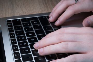 Young Caucasian woman's hands work on the keyboard of a laptop computer.
