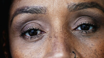 One black hispanic middle-aged 50s woman macro close-up eyes looking at camera with solemn serious...