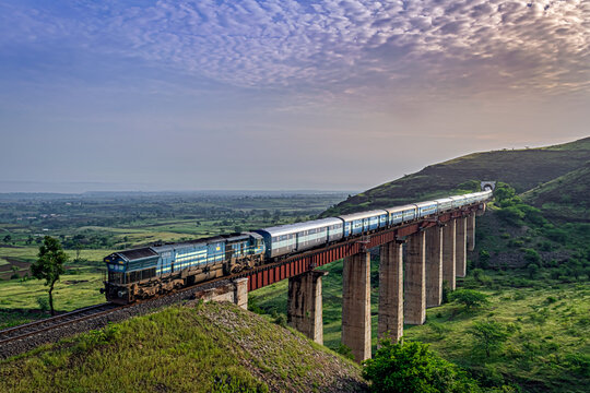 Along with Sunrise, Indian railways long passenger train, exiting a tunnel to cross a tall railway bridge.