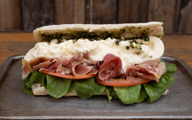 Closeup view of a gourmet sandwich with ciabatta bread, prosciutto ham, pesto sauce, burrata cheese...