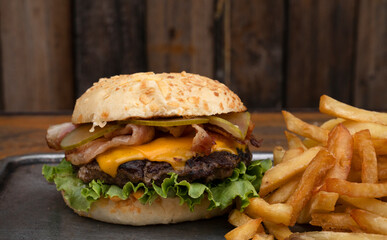 American food. Closeup view of a burger with grilled meat, lettuce, cucumber pickles, cheddar cheese, crispy bacon and french fries.	
