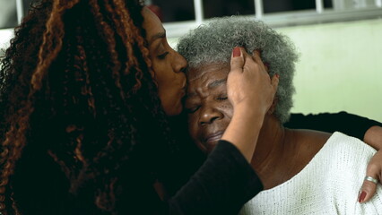 Tender loving moment of African American adult daughter kissing elderly 80s senior mother in the...