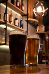 Happy hour. Closeup view of two beers, a golden one and a black stout one, on the wooden counter inside the English bar	
