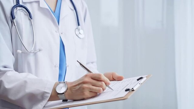 Female doctor taking notes on clipboard. Close-up of a unrecognizable female healthcare professional writing and filling um medication history records form while standing straight in clinic