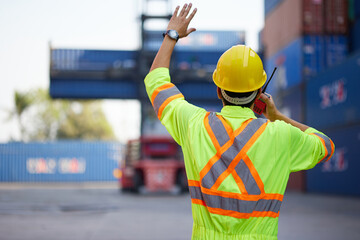 back view worker or engineer using walkie talkie and showing gesture to crane car in containers...