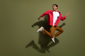 Full length photo of funky excited guy wear red shirt jumping high running empty space isolated khaki color background
