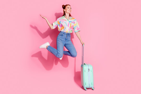 Naklejki Full size photo of attractive girl colorful blouse jump hold suitcase palm hold offer look empty space isolated on pink color background