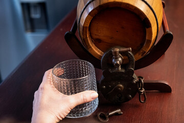 Left hand of a person holding an empty cup in front of a barrel with padlock and key