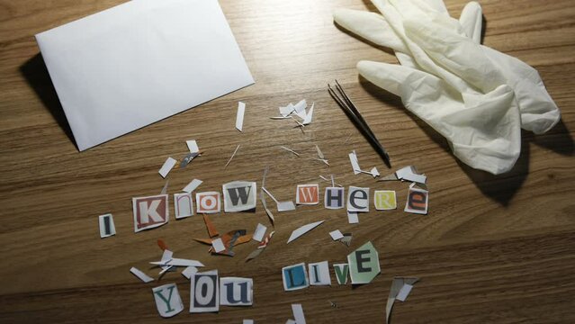 Letters cut out from newspapers and magazines for anonymous letters lie on the table. Creating an anonymous paper letter with the text I know where you live. Camera movement from right to left.