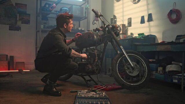 Professional auto mechanic repairing vintage motorbike using screwdriver in garage. Mechanic servicing or repairing vintage retro motorcycle in workshop. Maintenance and repair concept.