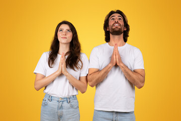 Hopeful couple with palms pressed together in prayer, looking upwards with contemplative expressions