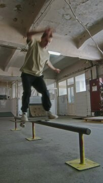 Vertical shot of young skilled skateboarder performing frontside boardslide trick at indoor skatepark