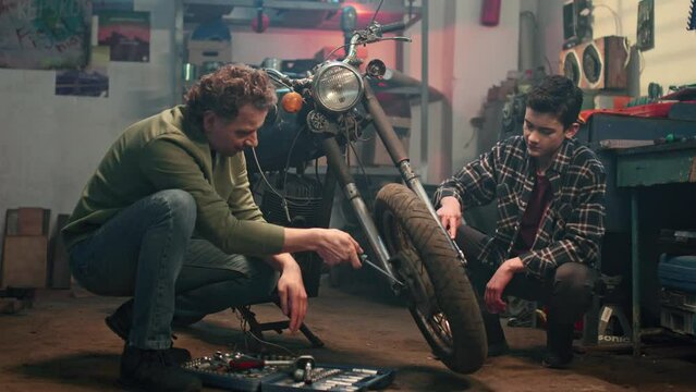 Professional repairman and young boy working in home garage. Mechanic servicing or repairing vintage retro motorbike with son in workshop. Maintenance service and small family business concept.