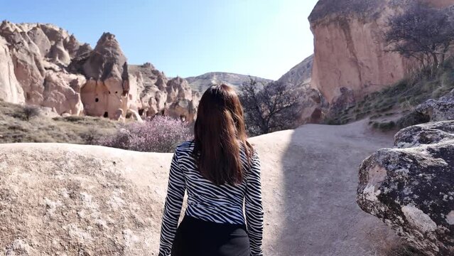 Woman takes a walk between rocks on a path and enjoys the scenery of the valley filled with fairy chimneys in Cappadocia.