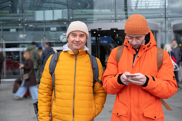 two men in orange jackets at station, Passengers with backpacks wait for train at station Berlin...