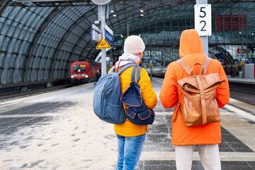two men in orange jackets at station, Passengers with backpacks wait train, Berlin Hauptbahnhof,...