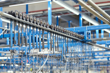 A metal roller rail in a textile factory industrial setting. Metal oil hangers on metal rollers. Cotton sewing and fabrication textile industries. Metal hanger rails.