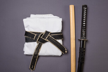 White kimano with a black belt and training weapons for fencing and martial arts on a gray...