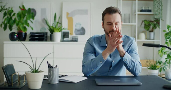 Worried businessman closing laptop sitting with hands clasped