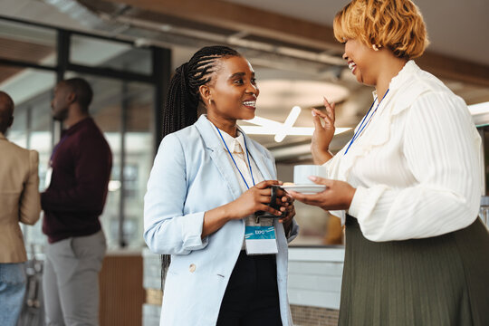 Professional women networking at a business conference, holding coffee and chatting