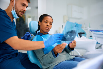 Black woman and her orthodontist looking at dental X-ray during appointment at dental clinic.