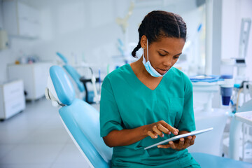 Black female dentist working on digital tablet at dental clinic - obrazy, fototapety, plakaty