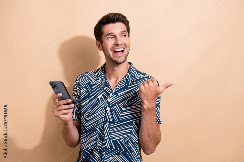 Poster photo of cheerful pleasant man dressed print shirt hold smartphone look directgin at logo empty spac
