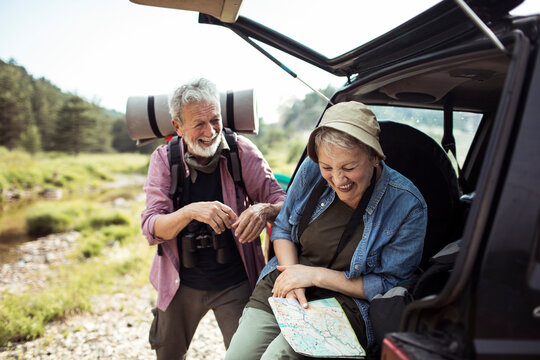 Senior couple laughing and looking at map on a hiking car trip