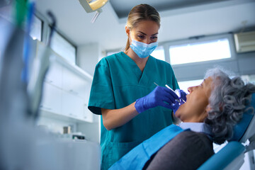 Female dentist examining teeth of senior woman at dentist's office.