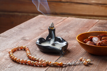 On the table are steaming incense, dates and Ramadan rosaries