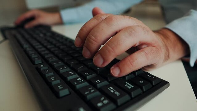 Primer plano de las manos en el teclado del hombre con camisa azul claro trabajando en la oficina, escribiendo